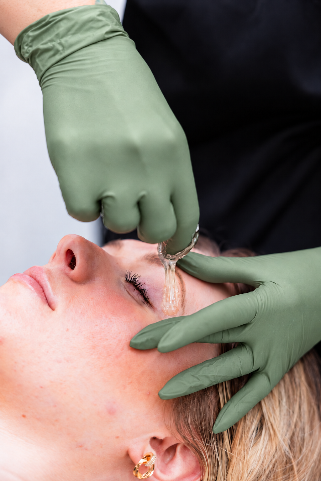 Professional eyebrow sugaring with muted sage-green gloves